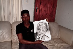 Photo of a young man sittng on a bed holding up a drawing